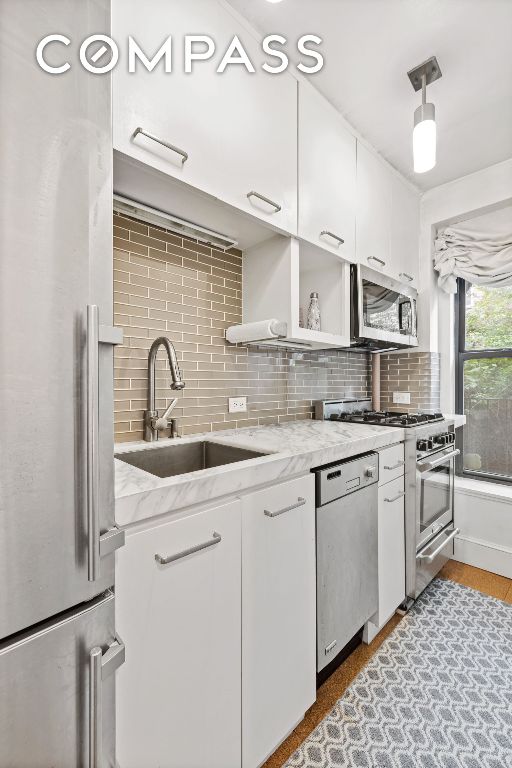 kitchen with appliances with stainless steel finishes, sink, white cabinets, backsplash, and light stone countertops