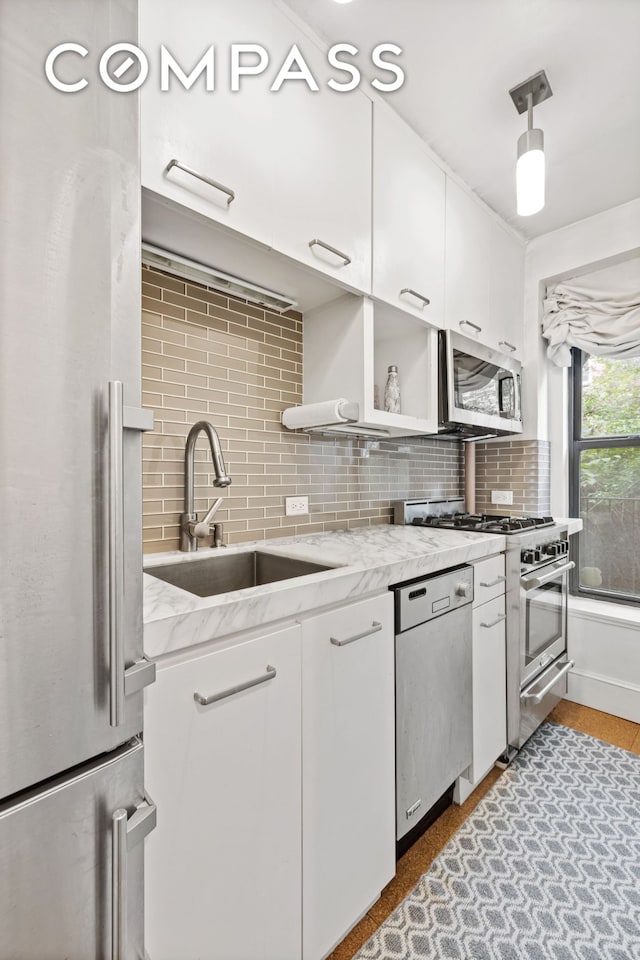 kitchen featuring light stone counters, a sink, decorative backsplash, appliances with stainless steel finishes, and white cabinetry