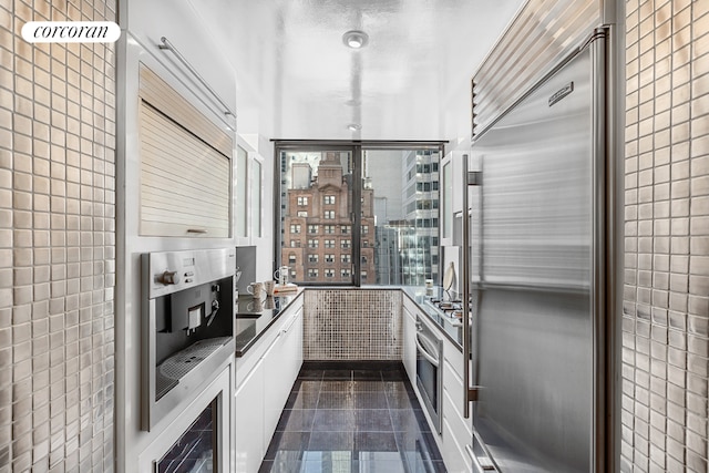 kitchen featuring white cabinetry, dark tile patterned flooring, stainless steel appliances, and tile walls