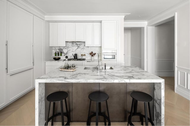 kitchen with a breakfast bar, sink, light parquet floors, and white cabinets