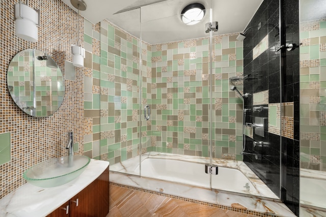 bathroom featuring bath / shower combo with glass door, tile walls, tasteful backsplash, and vanity