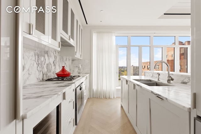 kitchen featuring light stone countertops, a sink, white cabinets, glass insert cabinets, and tasteful backsplash