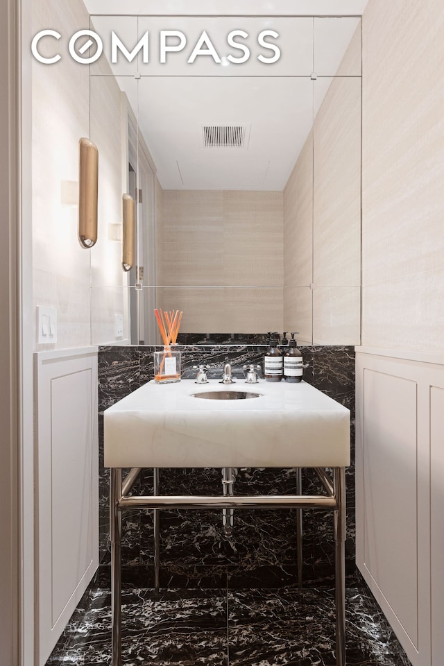 bathroom with a sink, visible vents, marble finish floor, and a decorative wall