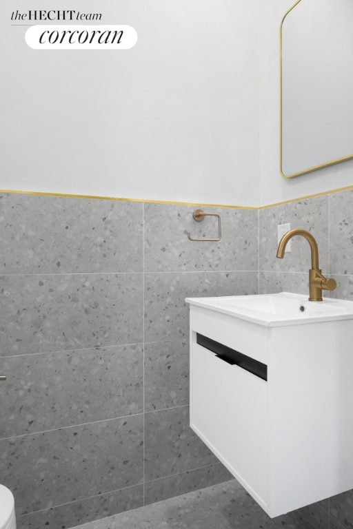 bathroom featuring toilet, vanity, and tile walls