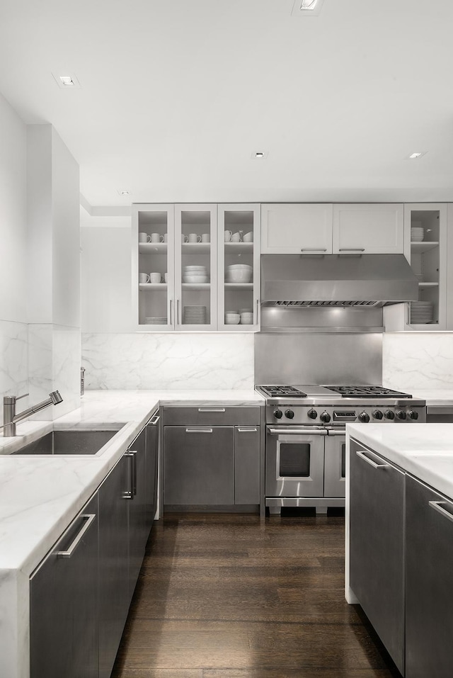 kitchen featuring a sink, under cabinet range hood, white cabinetry, range with two ovens, and light stone counters
