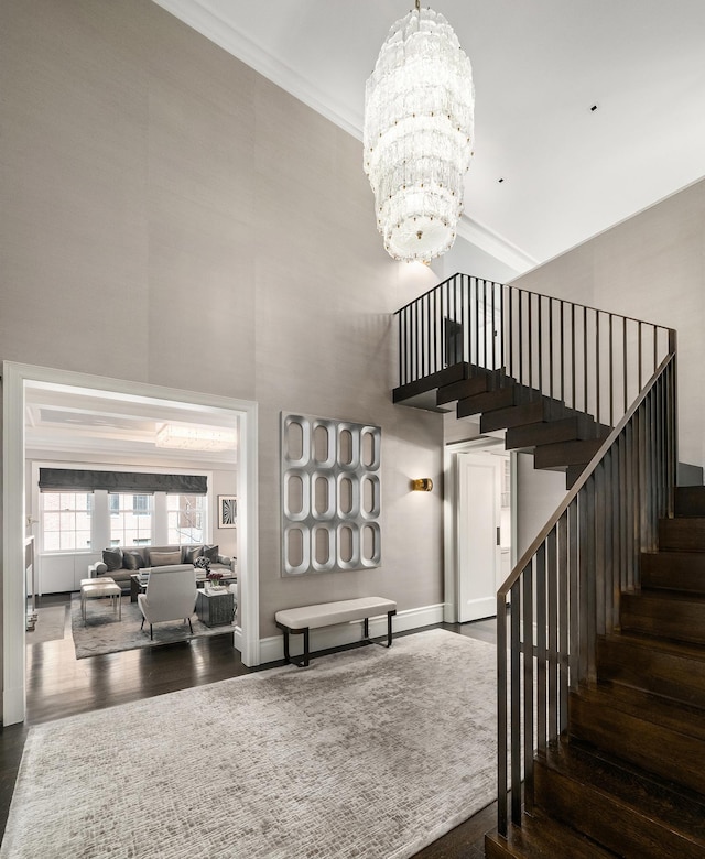 stairway featuring a chandelier, ornamental molding, a high ceiling, and wood finished floors