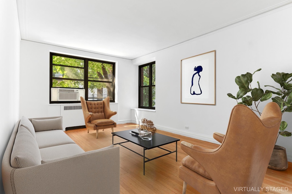 living area with radiator heating unit, wood finished floors, baseboards, and cooling unit