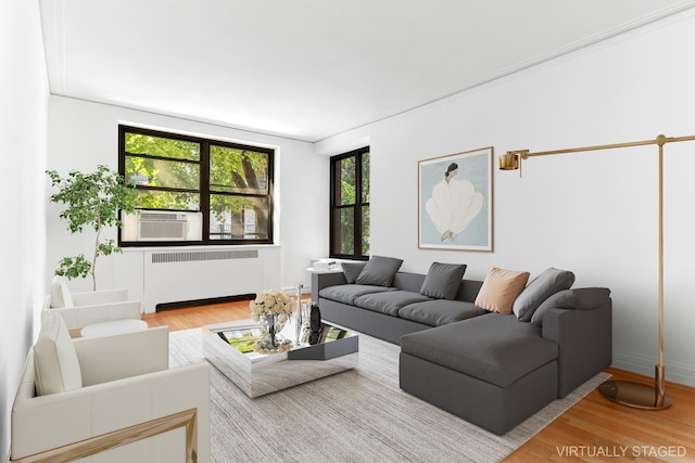living area with radiator heating unit, wood finished floors, baseboards, and cooling unit