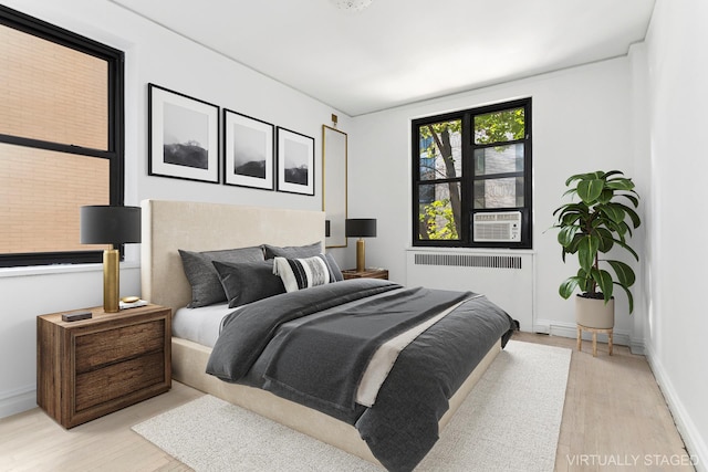 bedroom featuring radiator, light wood-style flooring, baseboards, and cooling unit
