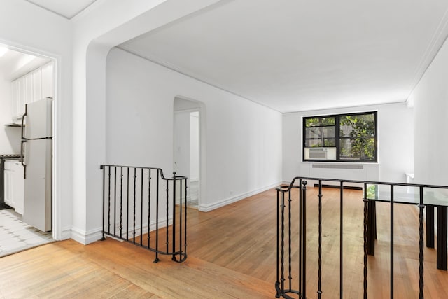 hallway featuring an upstairs landing, light wood finished floors, arched walkways, baseboards, and ornamental molding