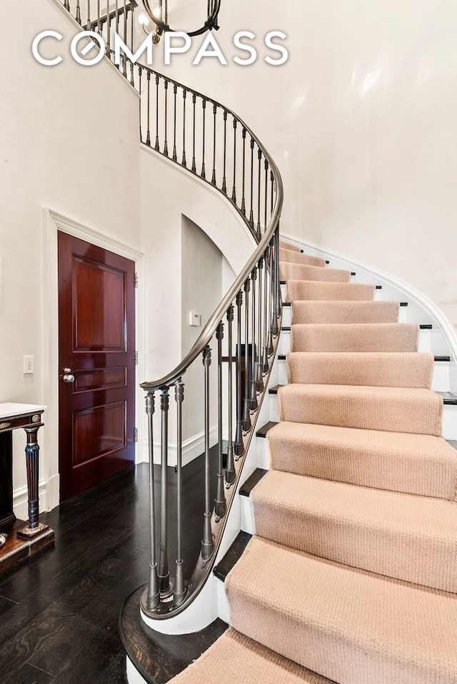 staircase featuring baseboards, a high ceiling, an inviting chandelier, and wood finished floors