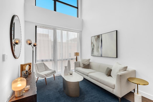 living room featuring a towering ceiling, wood finished floors, and baseboards