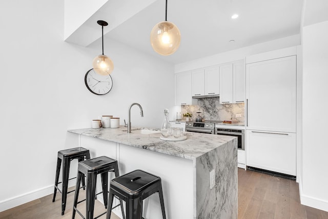 kitchen featuring a sink, a peninsula, white cabinets, backsplash, and wood finished floors