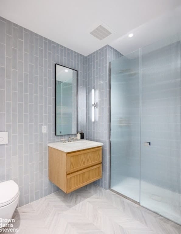 bathroom featuring tile walls, toilet, a shower with door, and vanity