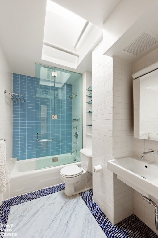 bathroom with combined bath / shower with glass door, tile walls, and toilet