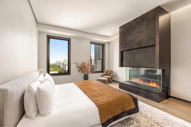 bedroom with a multi sided fireplace and light hardwood / wood-style floors