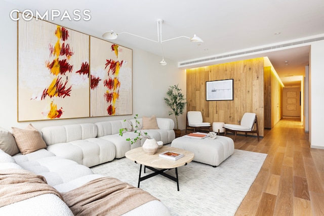 living area featuring light wood finished floors, wood walls, and visible vents