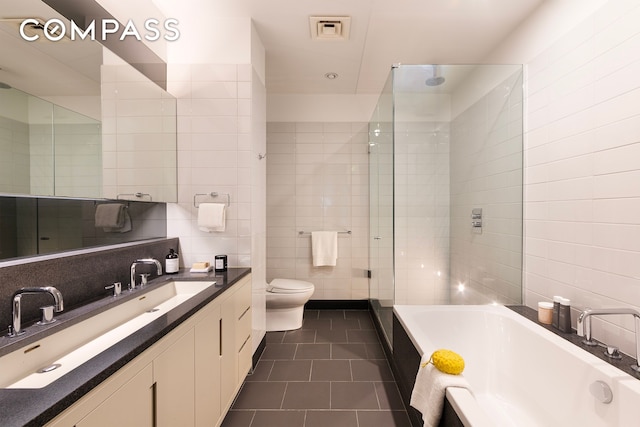 bathroom featuring toilet, visible vents, tile walls, tile patterned floors, and a bathtub