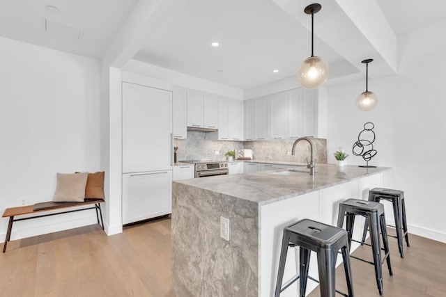 kitchen with sink, light stone counters, decorative light fixtures, kitchen peninsula, and white cabinets