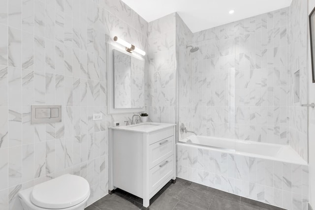 bathroom with tile walls, toilet, tiled shower / bath combo, vanity, and tile patterned flooring