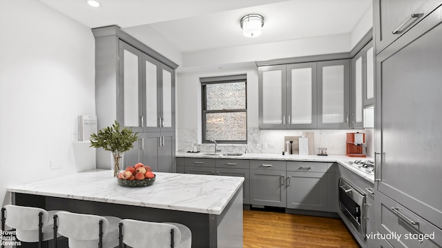 kitchen with a peninsula, a sink, oven, gray cabinetry, and a kitchen bar