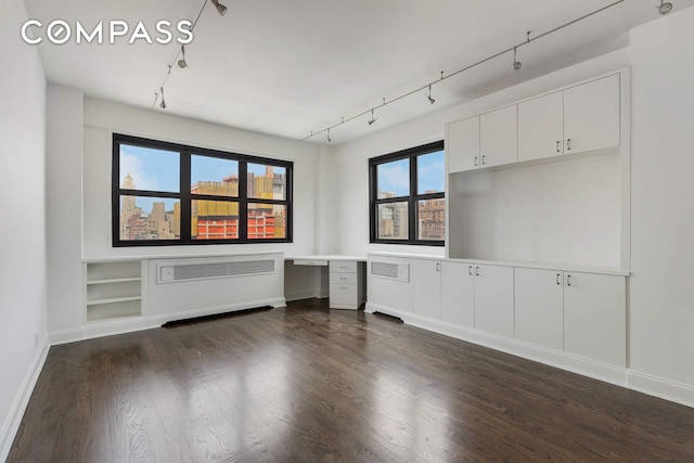 unfurnished living room with dark wood-style floors, radiator, rail lighting, and baseboards