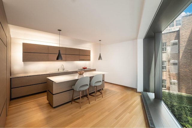 kitchen featuring a kitchen bar, a center island, decorative light fixtures, light wood-type flooring, and sink