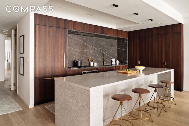 bar featuring tasteful backsplash, sink, dark brown cabinetry, and light wood-type flooring