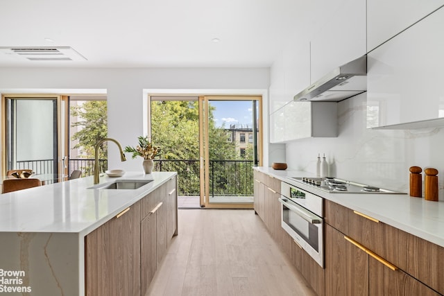 kitchen featuring light hardwood / wood-style floors, an island with sink, stainless steel appliances, white cabinets, and sink