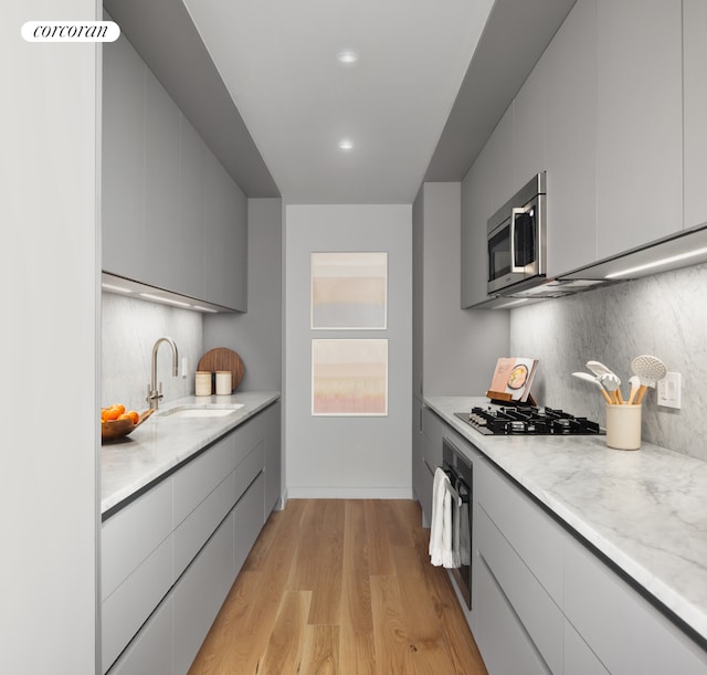 kitchen with light wood finished floors, a sink, decorative backsplash, black appliances, and modern cabinets