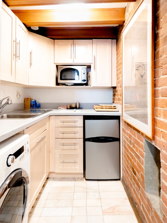 kitchen featuring washer / dryer, light tile patterned floors, appliances with stainless steel finishes, brick wall, and sink