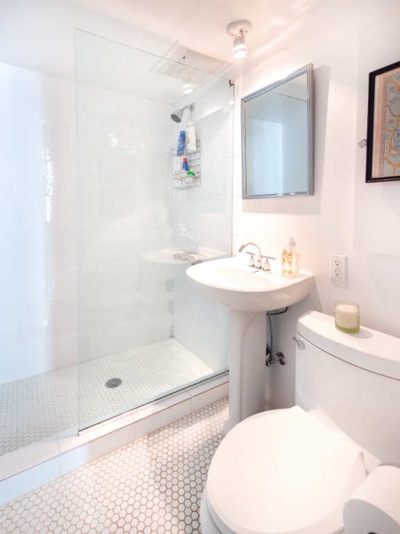 bathroom with toilet, tile patterned floors, and a tile shower