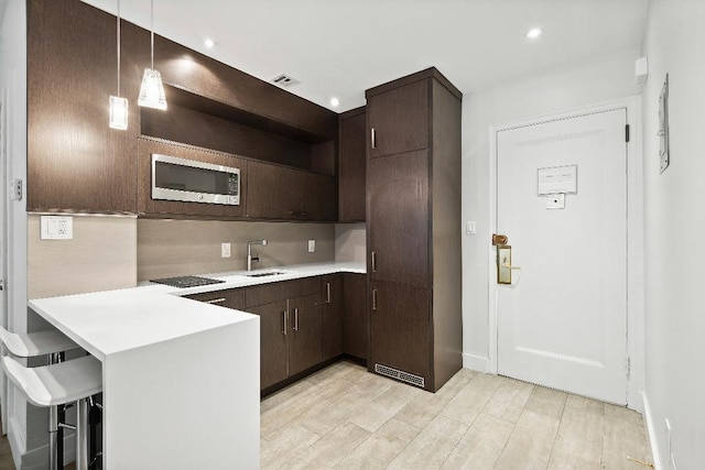 kitchen featuring a breakfast bar, hanging light fixtures, black gas cooktop, stainless steel microwave, and kitchen peninsula