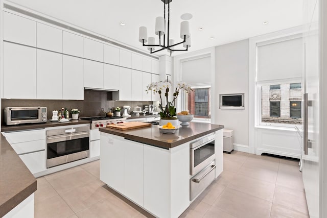 kitchen featuring a warming drawer, stainless steel appliances, dark countertops, white cabinets, and light tile patterned flooring