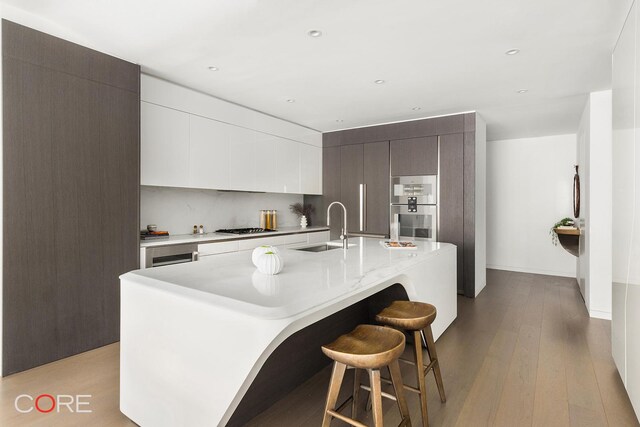 kitchen with sink, a breakfast bar, gas stovetop, a center island with sink, and light wood-type flooring