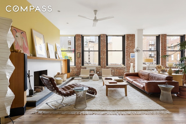 living room with brick wall, wood finished floors, and a ceiling fan