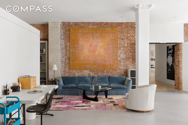 living area with decorative columns, brick wall, and finished concrete floors