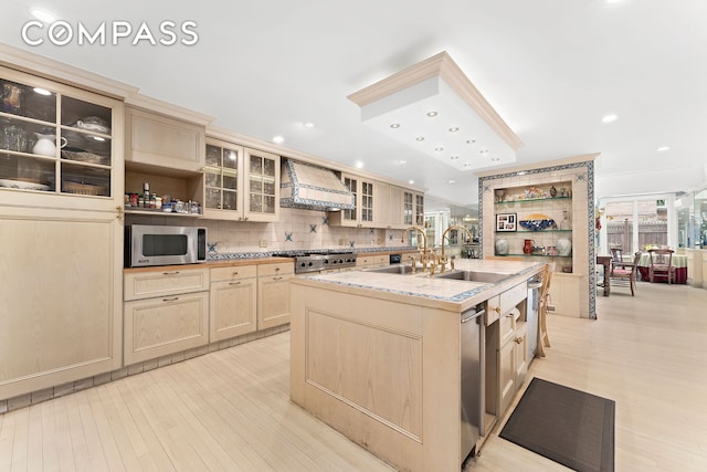 kitchen featuring premium range hood, a kitchen island with sink, open shelves, a sink, and appliances with stainless steel finishes