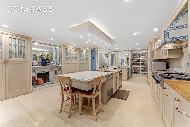 kitchen with light wood-style floors, stainless steel dishwasher, a large island with sink, gas stovetop, and a tile fireplace
