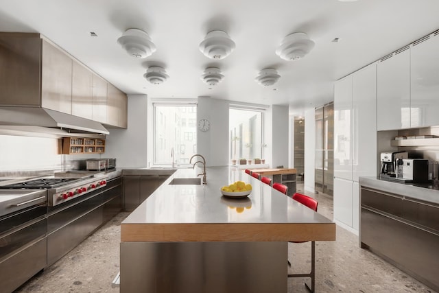 kitchen featuring modern cabinets, a breakfast bar area, a sink, stainless steel gas stovetop, and light speckled floor