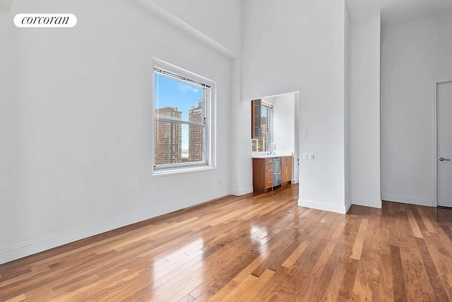 unfurnished bedroom with visible vents, baseboards, a high ceiling, light wood-style floors, and a sink