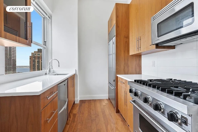 kitchen featuring brown cabinets, light countertops, decorative backsplash, appliances with stainless steel finishes, and a sink