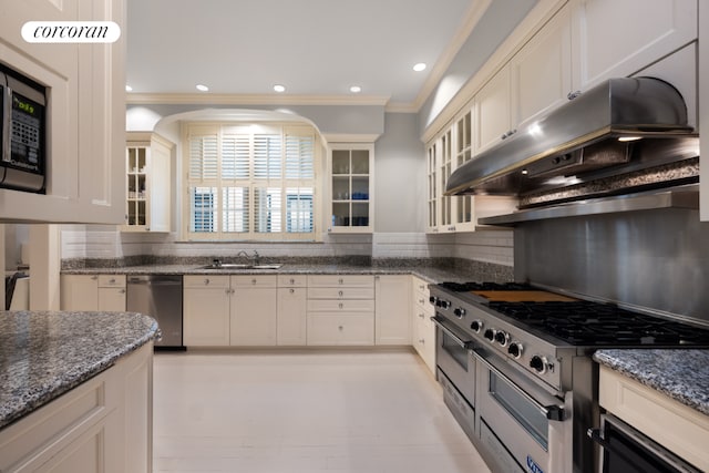 kitchen featuring dark stone counters, wall chimney range hood, crown molding, and stainless steel appliances