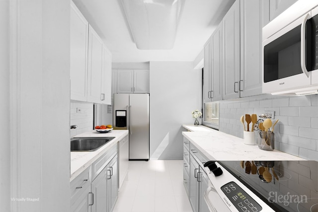 kitchen with sink, light stone counters, range with electric stovetop, stainless steel fridge, and backsplash