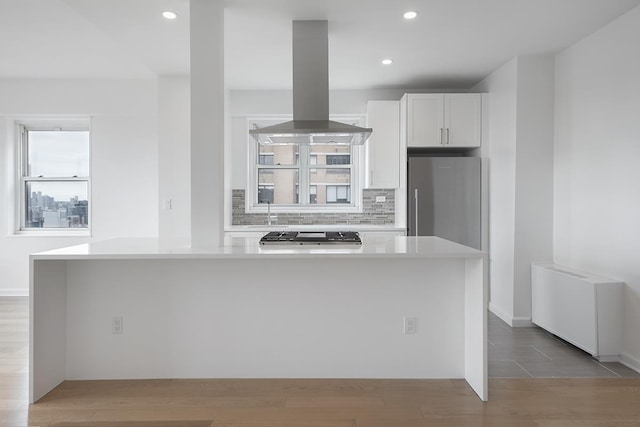 60 E 8th St Unit 27-N, New York City, NY 10003 - kitchen with island range hood, appliances with stainless steel finishes, backsplash, light countertops, and wood finished floors