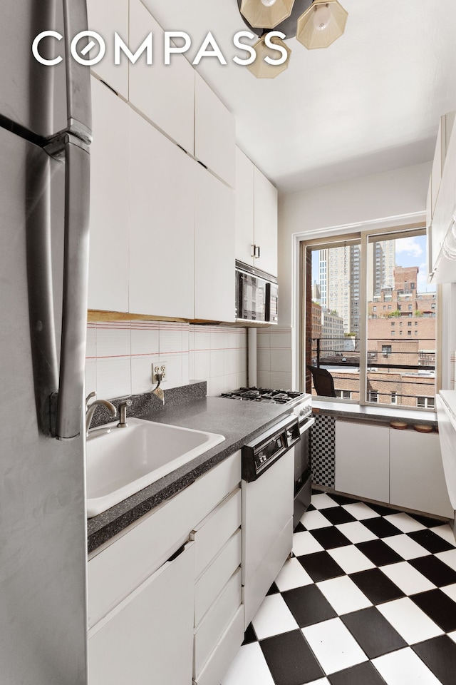 kitchen with white cabinets, dishwasher, a sink, light floors, and backsplash