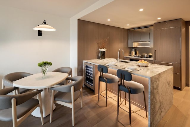 kitchen with light stone counters, light hardwood / wood-style floors, sink, and wine cooler