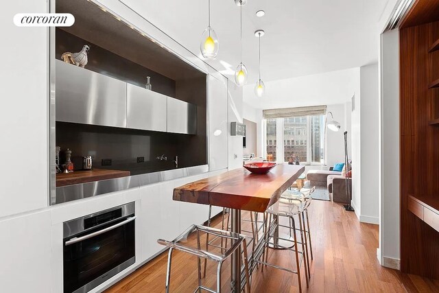 kitchen with white cabinets, a kitchen bar, oven, hanging light fixtures, and light wood-type flooring