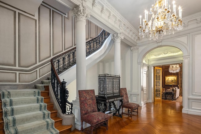 entrance foyer featuring arched walkways, a notable chandelier, a decorative wall, stairs, and ornate columns