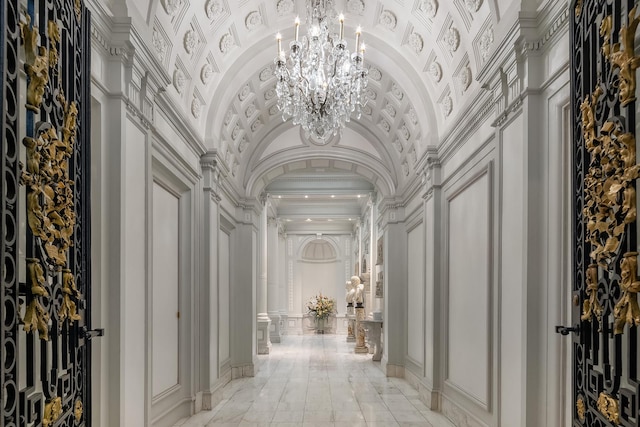 corridor featuring an inviting chandelier, ornamental molding, vaulted ceiling, and a decorative wall